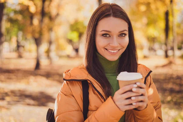 Energy pause. Photo of charming cute lady smiling hold cup drink visit coffee shop make break between university classes wear rucksack green turtleneck orange windbreaker outdoors