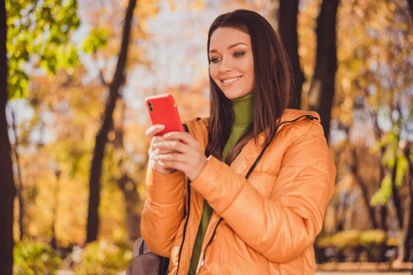 Photo of charming lovely young girl smiling hand hold telephone read weather prognosis good news want meet friend autumn park wear backpack green pullover orange coat trousers outside — Stock Photo, Image