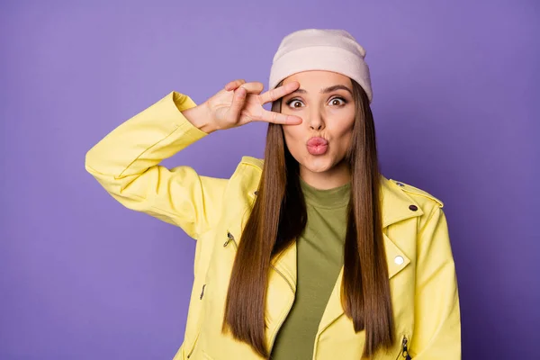 Foto de señora bastante agradable buen humor que muestra símbolo v-signo cerca del ojo que envía besos de aire desgaste chaqueta de cuero amarillo brillante camisa verde gorra moderna aislado pastel color púrpura fondo — Foto de Stock