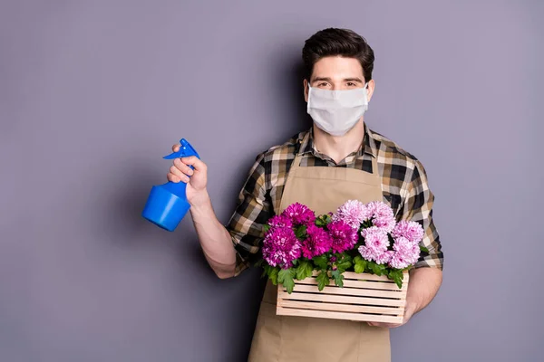 Retrato de seu jardineiro cara agradável usando máscara de segurança segurando em mãos flores pote plantas molhando parar a infecção mers doença cov isolado fundo cor cinza — Fotografia de Stock