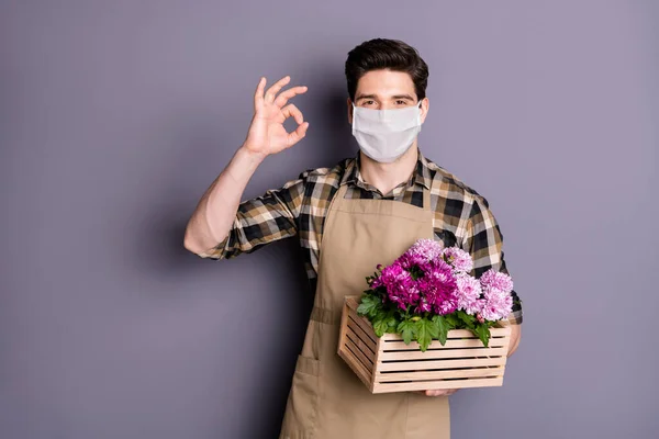 彼の素敵な健康的な男の庭師身に着けています安全マスクで手の花のポットストップ感染メーカーcov病気ショーok-sign隔離された灰色の背景 — ストック写真