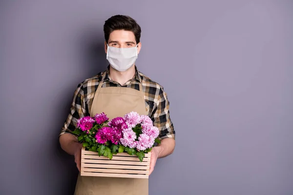 Πορτρέτο του ο καλός κηπουρός τύπος φορώντας μάσκα ασφαλείας κρατώντας στα χέρια λουλούδια γλάστρα σταματήσει μόλυνση mers cov προληπτικά μέτρα κοινωνική απόσταση παράδοση απομονωμένο γκρι χρώμα φόντο — Φωτογραφία Αρχείου