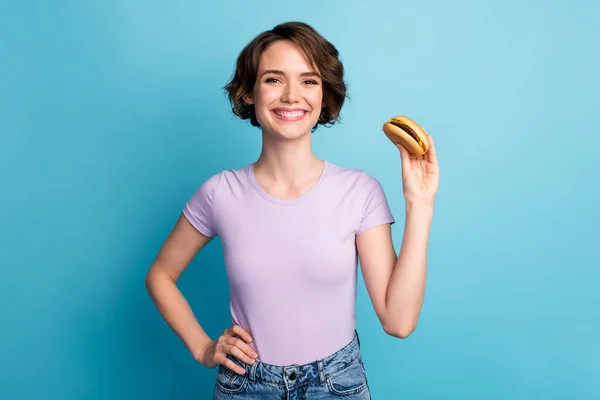 Foto de menina alegre positivo comer fast food hambúrguer desgaste boa aparência roupas isoladas sobre fundo de cor azul — Fotografia de Stock