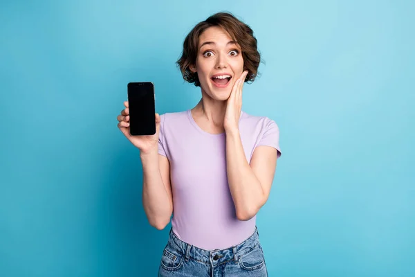 驚きの正の女の子の写真は、スマートフォンの印象的な近代的な技術割引タッチ手の顔は青い色の背景に隔離された良い外観の服を着用保持 — ストック写真
