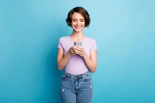 Foto van positieve vrolijke meisje gebruik smartphone genieten van lezen repost delen sociaal netwerk nieuws dragen lila violet t-shirt geïsoleerd over blauwe kleur achtergrond — Stockfoto