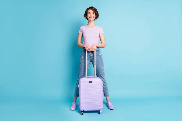 Полная длина фото позитивной веселой девушки турист пользуются поездки за границу провести чемодан носить сиреневый костюм кроссовки изолированы на синем фоне цвета — стоковое фото
