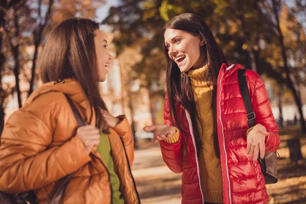 Photo of two girls best buddies have fun in autumn city town park tell say college amazing news hold bag wear outerwear bag