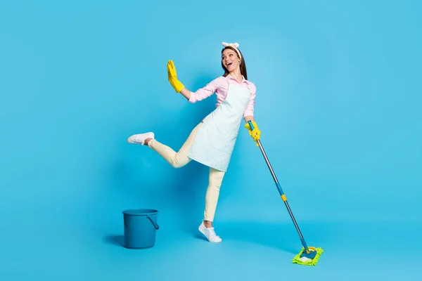 Volledige foto van positieve energieke meisje wassen vloer dweil stel je voor dat ze danseres dans dragen latex handschoenen roze shirt broek hoofdband geïsoleerd over blauwe kleur achtergrond — Stockfoto