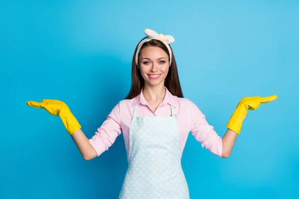 Portret van positieve schonere meisje houden hand aanwezig advertenties promotie optie object dragen roze shirt hoofdband geel latex handschoenen geïsoleerd over blauwe kleur achtergrond — Stockfoto