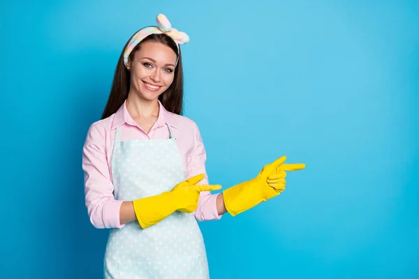 Foto van aantrekkelijke dame huis vrouw meid latex handschoenen handen lente schoonmaken regisseren vingers kant lege ruimte tonen aanbod dragen hoofdband gestippelde schort shirt geïsoleerde blauwe kleur achtergrond — Stockfoto