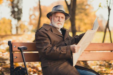 Photo of serious old man grumpy pensioner dont like kids play autumn town park sit bench read look newspaper wear cap long jacket outerwear clipart