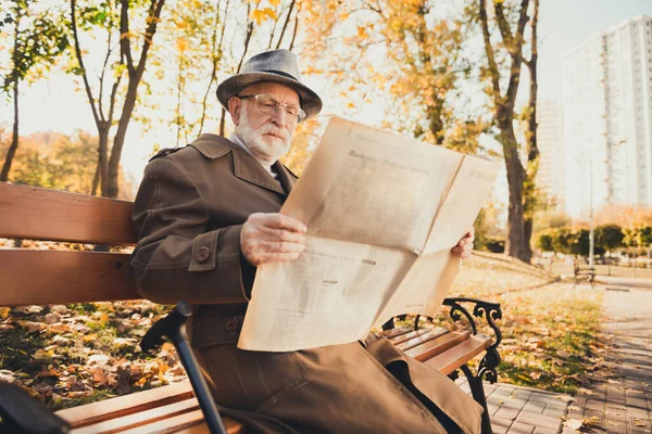 Photo de repos concentré vieil homme relax automne centre ville parc assis banc lire magazine vérifier nouvelles actuelles porter de longs vêtements de dessus — Photo