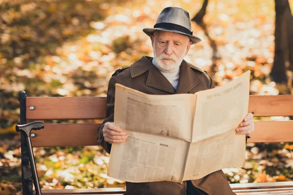 Photo de vieil homme concentré banc assis grand-père automne ville parc lire intéressant acheté journal porter casquette casque — Photo
