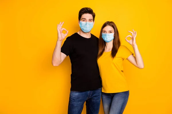 Retrato dele ele ela ela agradável atraente casal saudável mostrando ok-sinal abraçando vestindo máscara de segurança parar mers cov doença infecção prevenção isolado vibrante cor amarela fundo — Fotografia de Stock