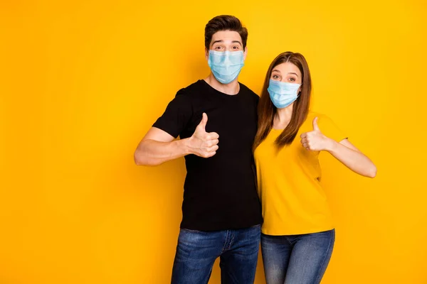 Portrait of his he her she nice attractive healthy couple showing thumbup wearing safety mask stop pandemia mers cov influenza prevention isolated vibrant yellow color background — Stock Photo, Image