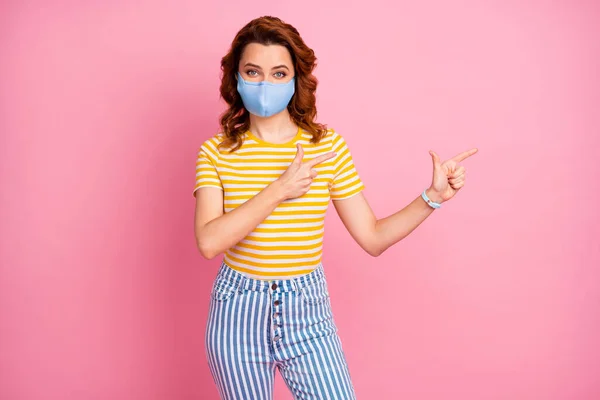 Retrato dela ela agradável atraente menina de cabelos ondulados saudável vestindo máscara têxtil reutilizável demonstrando espaço de cópia parar diagnóstico influenza isolado cor pastel rosa fundo — Fotografia de Stock