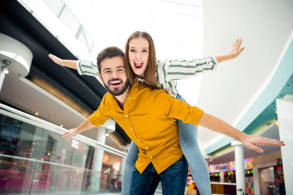 Baixo ângulo ver foto de senhora engraçado espalhar braços como asas cara bonito levar seu lazer piggyback shopping center juntos bom humor se divertindo conhecer aventuras usar roupas casuais dentro de casa — Fotografia de Stock