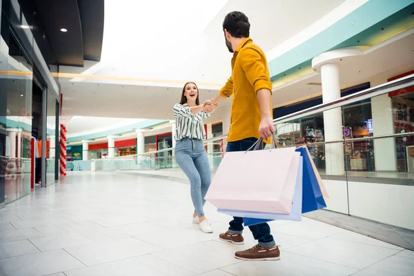 Vamos, cariño. Foto de longitud completa de alegre señora bonita plomo manos chico guapo a la próxima tienda quiere comprar una camisa más zapatos de vestir muchos bolsos centro comercial desgaste traje casual en el interior — Foto de Stock