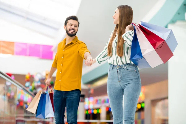 Retrato de pareja soñadora alegre positiva hombre mujer ir a caminar en el centro comercial centro comercial disfrutar de la diversión tiempo libre celebrar bolsas paquetes celebrar mano desgaste camisa amarilla rayas vaqueros — Foto de Stock