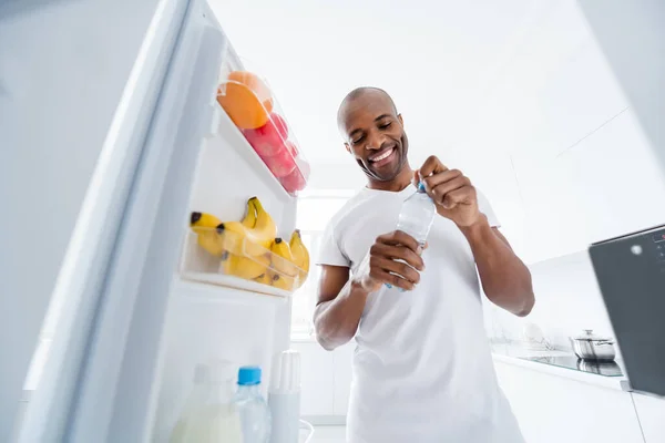 Портрет його привабливого веселого веселого здорового хлопця, який приймає в холодильнику свіжу їжу напої мінеральні артезіанські води в світло-білій кухні інтер'єру будинку в приміщенні — стокове фото