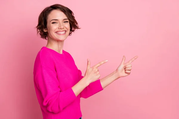 Photo of overjoyed excited lady toothy smiling directing fingers side empty space showing novelty sale discount banner wear casual bright sweater isolated pink pastel color background