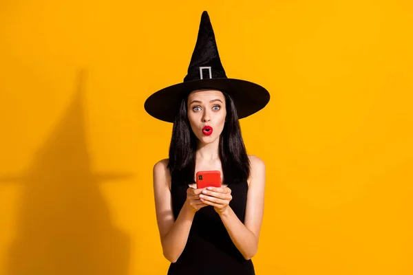 Halloween hampir dibatalkan. Foto pesulap muda yang cantik ini mengadakan acara telepon dengan tema yang mengagumkan sambil menunda mengenakan pakaian penyihir hitam dengan latar belakang berwarna kuning cerah yang terisolasi — Stok Foto