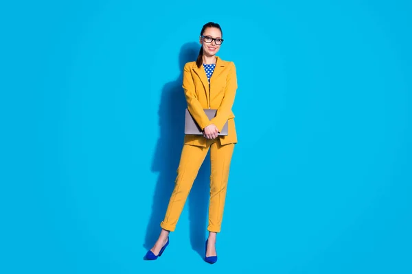 Фотографія привабливої ділової леді працівник тримає ноутбук онлайн зустріч одягнений в окуляри жовтий костюм блейзер пунктирна блузка сорочка на високих підборах ізольований яскраво-синій кольоровий фон — стокове фото