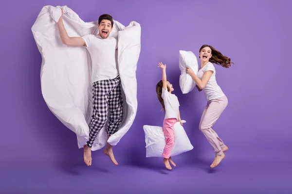 Full length body size view of cheerful glad crazy family small little daughter jumping carrying pillow duvet having fun bedtime isolated on bright vivid shine vibrant violet color background