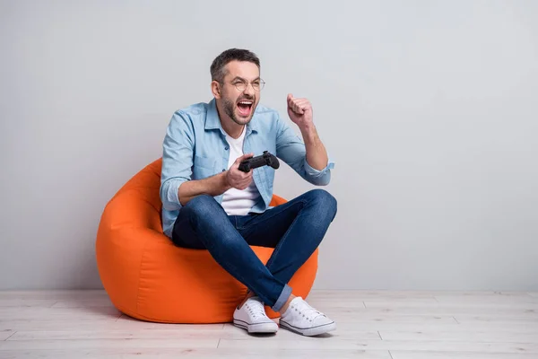 Portret van zijn hij mooie aantrekkelijke vrolijke vrolijke overjoyed grijs-harige man zitten in zak stoel spelen spel plezier besteden vrije tijd geïsoleerd over grijs licht pastel kleur achtergrond — Stockfoto