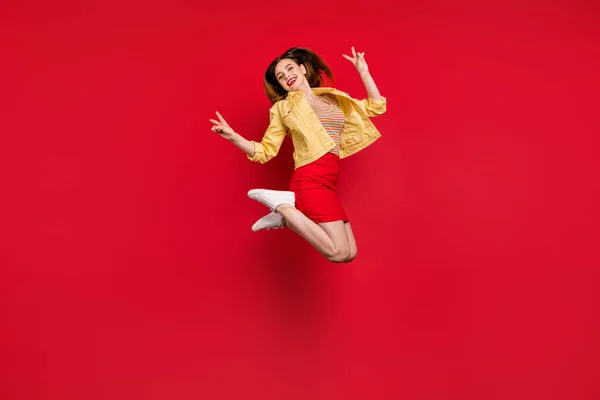 Çekici bayanın tam boy fotoğrafı iyi ruh hali yükseğe zıplıyor V işaretli eller gösteriyor sarı ceket giyiyor kısa etek, izole edilmiş kırmızı arka plan — Stok fotoğraf