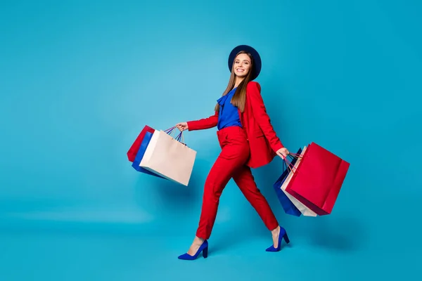 Full body profile photo of confident lady boss walk shopping center hold many packs wear retro cap red suit shirt blazer pants high-heels isolated blue color background — Stock Photo, Image