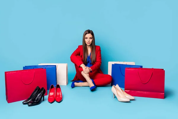Полнометражное фото самоуверенной женщины успешной работницы, сидящей рядом с обувью сумки для покупок носить блузку в красном костюме брюки пиджака на высоких каблуках изолированный синий цвет фона — стоковое фото