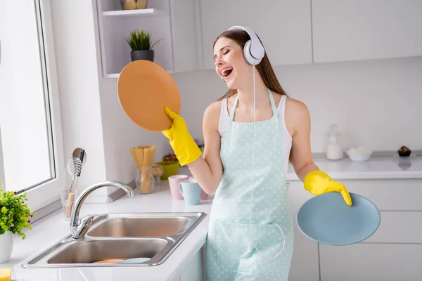 Foto gadis ceria positif mengadakan layanan cuci piring bersih mendengarkan lagu headset menikmati pekerjaan membersihkan sukacita mengenakan sarung tangan lateks kuning di rumah dapur di dalam ruangan — Stok Foto