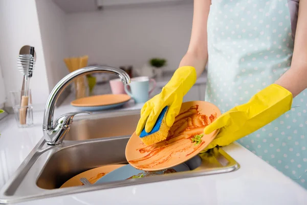Recorte de perto foto de mulher empregada doméstica lavar pratos sujos após refeição fresca orgânica saborosa usar esponja usar luvas de látex amarelo na casa de cozinha em casa — Fotografia de Stock