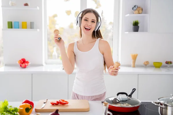 Foto de menina alegre positiva chef gourmet ouvir fone de ouvido dança segurar pimenta sal imagine que ela salsa festa dançarina em casa de cozinha em casa — Fotografia de Stock