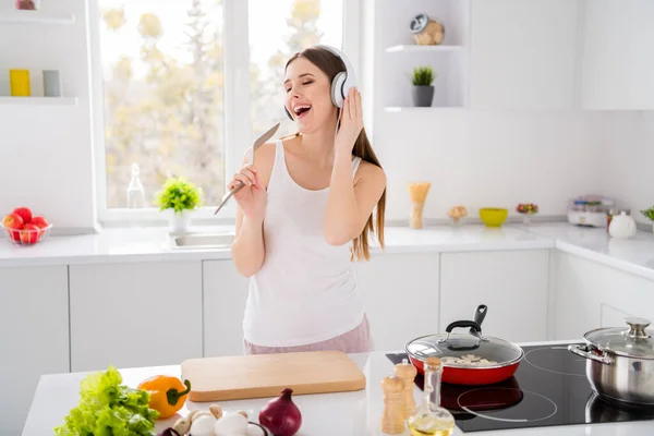 Foto van positief meisje bereiden avondeten ecologisch recept luisteren headset ritmische muziek gebruik spatel zingen lied melodie als beroemde zanger in huis keuken binnen — Stockfoto