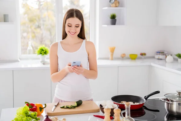 Foto de chica positiva uso de chef preparar ensalada orgánica sabrosa cena usar smartphone cocina culinaria blogging en casa cocina interior — Foto de Stock