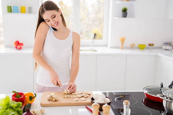 Фото позитивної дівчини готують смачну кулінарну вечерю нарізання грибів ножем розмовляти смартфон з другом в кухонному будинку в приміщенні — стокове фото