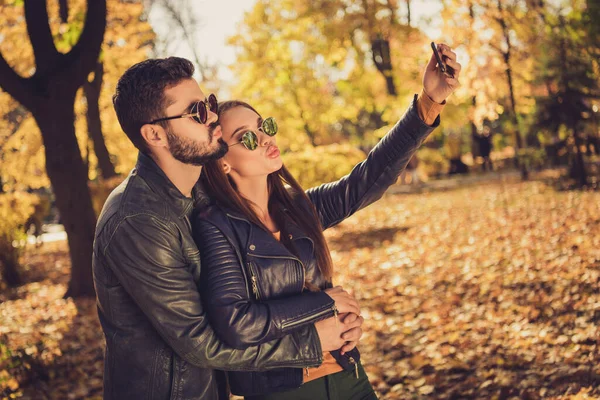 Photo of two people students girl guy hug make selfie on smartphone send air kiss in fall September park wear jacket — Zdjęcie stockowe