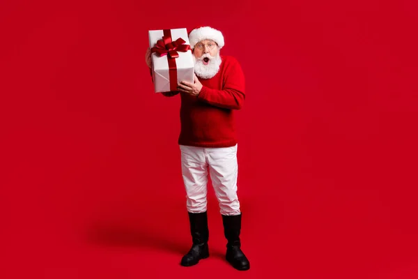 Ganzes Foto von erstaunt alten Mann in Santa Claus Kopfbedeckung halten große Geschenkbox beeindruckt Traum fröhlich Stechpalme anwesend tragen Pullover Hose Stiefel isoliert über hellen Glanz Farbe Hintergrund — Stockfoto