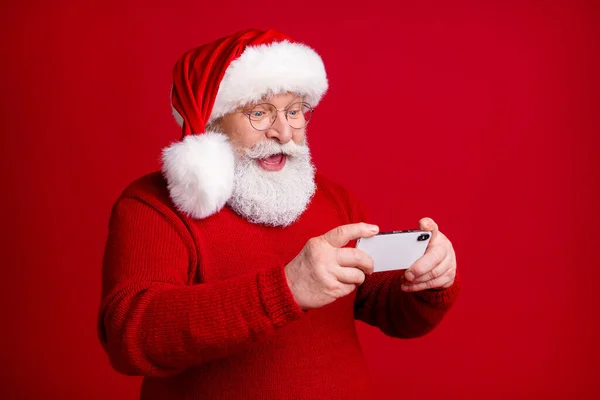 Foto de louco animado velho homem em santa claus headwear uso smartphone desfrutar x-mas alegre holly anúncios do ano novo usar camisola isolada sobre brilhante brilho cor fundo — Fotografia de Stock