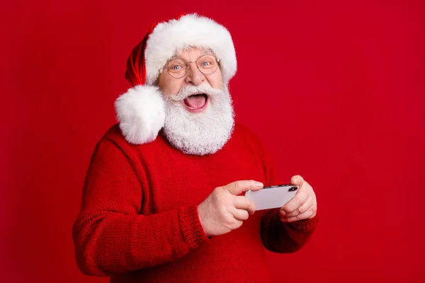 Foto de impressionado louco velho homem em santa claus headwear uso smartphone desfrutar x-mas mágica milagres descontos desgaste camisola jumper isolado sobre brilhante brilho cor fundo — Fotografia de Stock