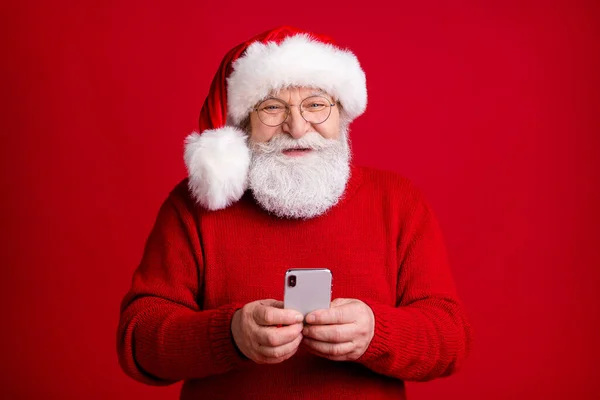 Foto av positiv gammal man i Santa claus huvudbonader använda smartphone njuta av följa x-mas glada järna rabatter bära tröja tröja tröja tröja isolerad över ljus glans färg bakgrund — Stockfoto