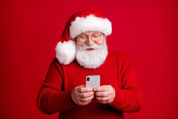 Eski fotoğrafçı, emekli, Noel Baba 'nın baş örtüsü giyen gri saçlı, akıllı telefon kullanan, sosyal medyayı takip eden, x-mas kutsal indirimli süveter giyen, parlak renkli arka plan giyen. — Stok fotoğraf