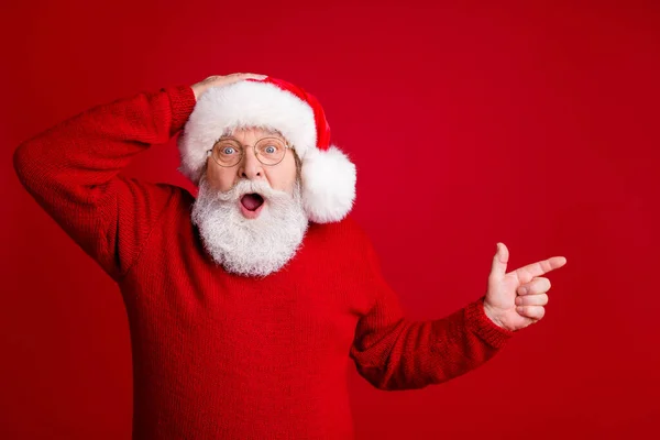 Foto van verbaasd grijs haar oude man in kerstman hoed punt index vinger copyspace onder de indruk vrolijke hulst x-mas advertenties promo slijtage trui geïsoleerd over heldere glans kleur achtergrond — Stockfoto