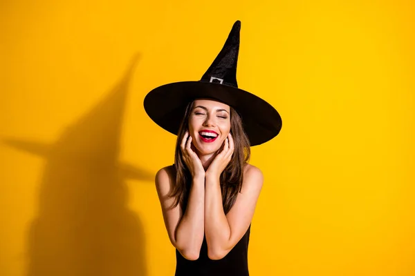 かわいいかなり若い女性の目を閉じて口の手の顔を聞いて非常に賞賛秋のテーマイベントは、黒魔女の衣装コーンヘッドウェア隔離された黄色の背景を身に着けている — ストック写真