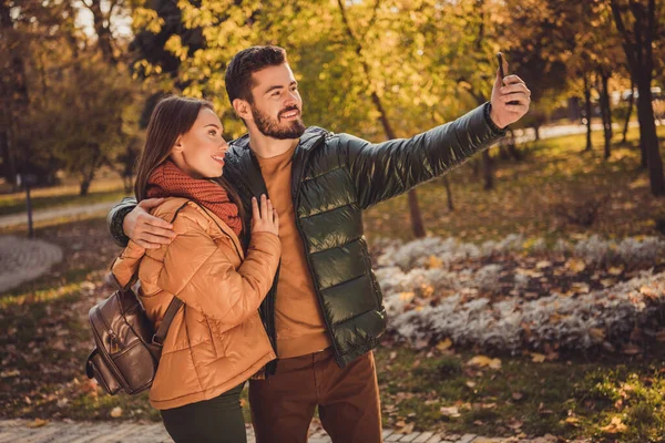 Olumlu iki kişinin fotoğrafı. İki öğrenci, kızı kucaklıyor. Sonbahar parkında akıllı telefondan selfie çekiyor. — Stok fotoğraf