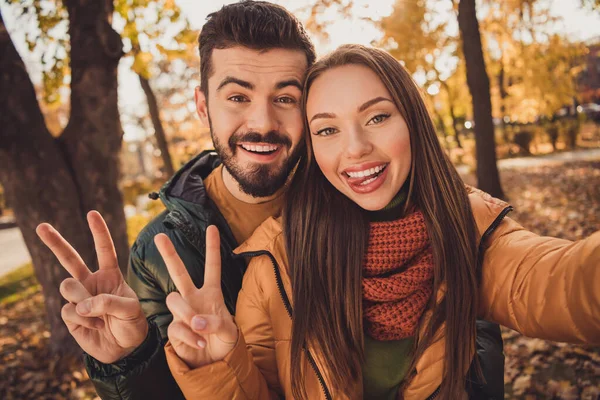 Portrait of positive two people students couple take selfie make v-sign symbol show tongue out in autumn park