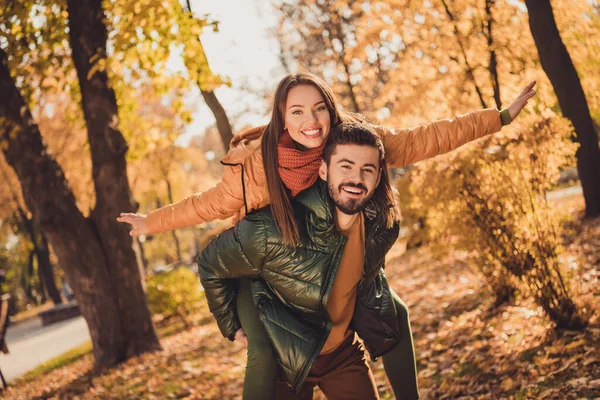 Φωτογραφία του ρομαντικό ζευγάρι τύπος κατέχουν piggyback κορίτσι με τα χέρια που φέρουν το φθινόπωρο του Οκτωβρίου πάρκο της πόλης φορούν παλτά — Φωτογραφία Αρχείου