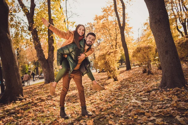 Full storlek foto av positiva par i höst September Forest Park kille hålla flicka piggyback bära oktober ytterkläder — Stockfoto